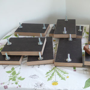 Auf einem Tisch mit einer Blumenmotivdecke liegen aus Siebdruckplatten gefertigte mit Schrauben und Muttern zusammengehaltene Pressen